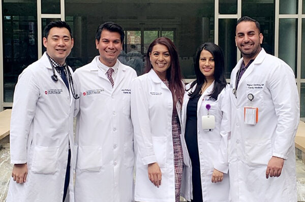 Five medical providers in white coats standing in a row