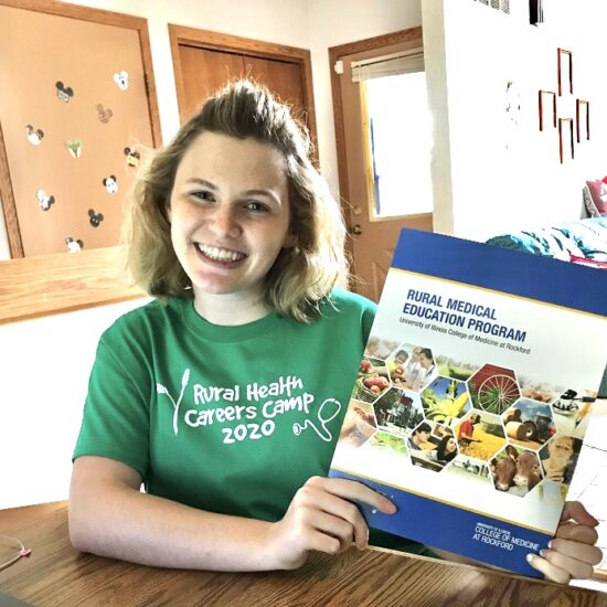 A student poses in a Rural Health Careers Camp tshirt with a brochure