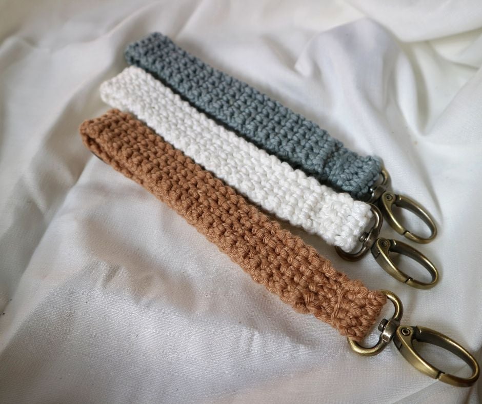 Three crocheted keychains in tan, white and blue on white fabric