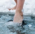 Toes dipped into icy water from the edge of a snow covered beach